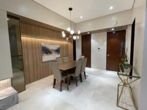 Modern dining area with a wooden table and six beige chairs, contemporary chandelier above, wall art, and wooden wall paneling. A console table with decorative items sits to the right, showcasing a recent renovation that seamlessly blends comfort and style.