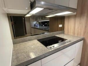 Modern kitchen with a smooth electric stovetop, stainless steel range hood, marble countertop, wooden cabinets, and a reflective backsplash. The space has built-in lighting and power outlets, exemplifying top-tier interior fit-out design and build expertise typically seen in upscale office settings.