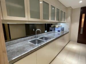 Modern kitchen with glossy beige cabinets, under-cabinet lighting, double stainless steel sink, marble countertop, and tile flooring. Perfect for a commercial office interior fit-out, the packs of kitchen appliances on the counter enhance its functionality.