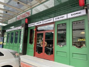 A restaurant with a green and red facade called "Red Mox" offers various dishes such as spareribs, dimsum, claypot, stir fry, and siomai. A car is parked in front of the storefront, blending seamlessly into the surrounding office buildings.