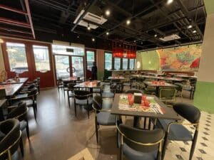 A modern restaurant with neatly arranged tables and chairs, colorful murals on the walls, and a person standing near the entrance, showcasing an exceptional interior fit-out that rivals even the most stylish office spaces.