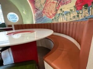 A semi-circular brown leather booth with a white table is set against a colorful wall mural featuring cityscapes and abstract designs, perfect for adding flair to any residential interior fit-out.