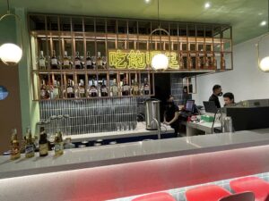 Modern bar with a white countertop, backlit with a neon sign and bottles on shelves. Three people are behind the bar counter, with some beer bottles placed on the counter. The design and build reflect a sleek, commercial aesthetic perfect for both residential and nightlife venues.