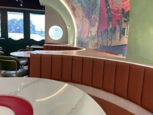 A modern cafe interior with curved seating, round marble tables, green chairs, and a colorful mural on the wall showcases a seamless interior fit-out.