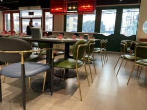 An empty modern indoor restaurant with green chairs, a black table, red ceiling lights, and large windows showcases impeccable design and build quality, almost resembling a chic office space.