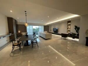 A spacious, modern open-plan living area with a dining table, chairs, sofas, a television, and large windows with curtains. This commercial interior fit-out features polished marble floors and contemporary lighting.