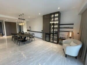 Modern dining area featuring a sleek black table with chairs, a tall cabinet with glass doors, minimalist shelves, and a cozy white armchair with a lamp. The residential space boasts polished marble floors and neutral decor, showcasing a thoughtful interior fit-out that elevates the overall ambiance.