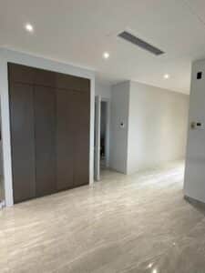 A minimalist, modern interior with large marble floor tiles, recessed lighting, a dark wood built-in cabinet on the left, and white walls showcases a recent residential renovation.