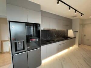 A modern kitchen featuring built-in gray cabinets, a black marble backsplash, an integrated refrigerator, and an under-cabinet lighting system showcases expert interior fit-out skills.