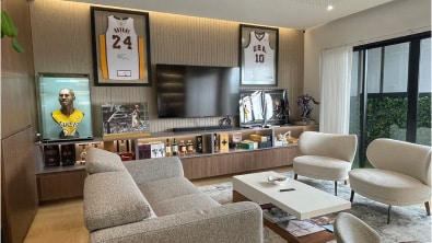 A modern living room with sports memorabilia, including framed basketball jerseys and a displayed bust, a large TV, and contemporary furniture including a sofa, armchairs, and a coffee table. This versatile space could easily serve as an inviting residential area or a stylish office lounge.