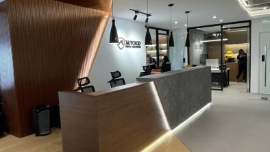 Modern reception area with a sleek desk, wooden accent wall, pendant lights, and visible office area in the background—thanks to a recent interior fit-out. Sign on the wall reads "Advanced Prosthetics.