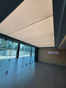 Modern showroom interior with glass walls, tiled floor, illuminated ceiling panels, and a BYD logo on a wooden accent wall.