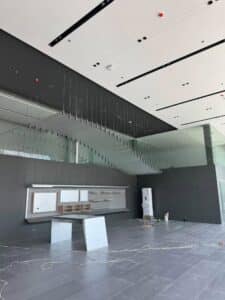 Modern interior space under construction with a floating glass staircase, unpacked furniture, exposed wires, and unfinished installation work.