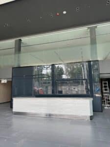 A modern, empty lobby with a large glass wall, a counter wrapped in protective material, black tiles, and a ladder on the right side.