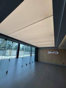 A modern interior with floor-to-ceiling glass doors, tiled flooring, a wood-paneled wall, and a BYD logo illuminated on the right side.