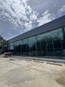 A modern glass-fronted building labeled "Bataan" under a partly cloudy sky, with construction materials and scaffolding visible in the foreground.