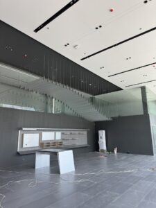 Modern interior space under construction with a floating staircase, built-in shelving, tiled floor, loose cables, and construction materials scattered around.