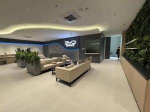 Modern waiting area with beige sofas, potted plants, and a "BYD Service" sign on the wall; a person stands near a doorway in the background.