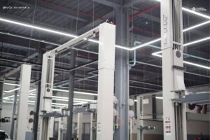 A car lift stands inside a modern, well-lit automotive service garage with exposed pipes and overhead lighting.