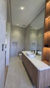 Modern bathroom with light grey tiles, a wall-mounted wooden vanity with a white vessel sink, large mirror, built-in shelf, and recessed spotlights.