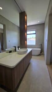 Modern bathroom with a wooden vanity and vessel sink, a freestanding bathtub near a window, and neutral-colored walls and floors.