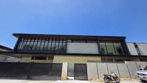 A modern two-story building with large glass windows, a gated entrance, and a parked motorcycle in front under a clear blue sky.