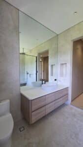 Modern bathroom with a large wall mirror, wooden vanity with two vessel sinks, and a walk-in shower visible in the background.