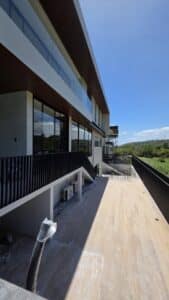 A modern multi-story building with large windows and a spacious wooden deck overlooking greenery under a clear blue sky.