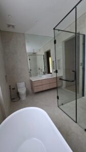 Modern bathroom with a glass shower enclosure, freestanding bathtub, wall-mounted toilet, large mirror, and floating vanity with drawers. Neutral-colored tiles cover the floor and walls.