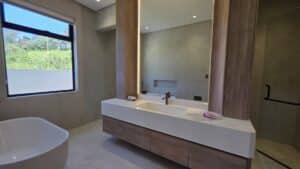 Modern bathroom with large mirror, double sink vanity, wood accents, freestanding bathtub, and a window providing natural light.