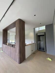 Modern kitchen with wood paneling and a built-in counter; a small residential elevator is installed in the corner of the open-plan room.