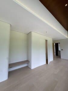 Minimalist modern interior with light wood flooring, white curved walls, a floating wooden shelf, and recessed ceiling lighting.