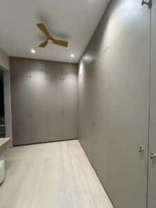 Modern walk-in closet with beige floor-to-ceiling cabinets, light wood flooring, recessed ceiling lights, and a yellow ceiling fan.